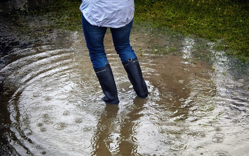 Photo of legs with rubber boots standing in a flooded yard