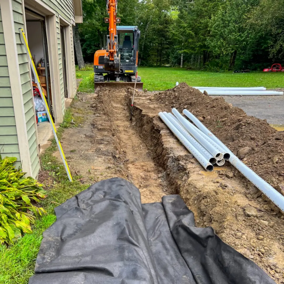 An excavator parked beside a trench with PVC pipes laid next to it near a house, indicating ongoing Hines Ground Services' underground utility work.