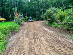 A bulldozer is working on a dirt road in a wooded area.