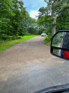 A side view mirror of a car driving down a dirt road.