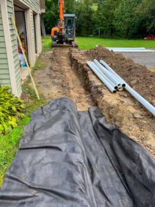 A black tarp is being used to cover a pipe in a yard.