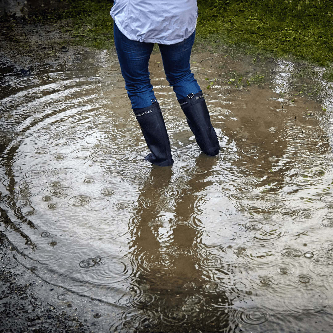 Photo of woman with rubber boots standing in a flooded yard due to poor drainage